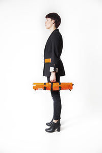 Sac Origami de la marque Dababo, sac pliable multi-fonctions, 3 positions en chutes de baches de camions recyclées porté de profil par une femme en format roulé de couleur orange.