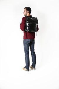Sac à dos noir Tyrolien , marque Dababo en chutes de baches de camion recyclées. Porté par un homme de dos. Grande contenance, fermeture par lien de serrage et rabat à Velcro.